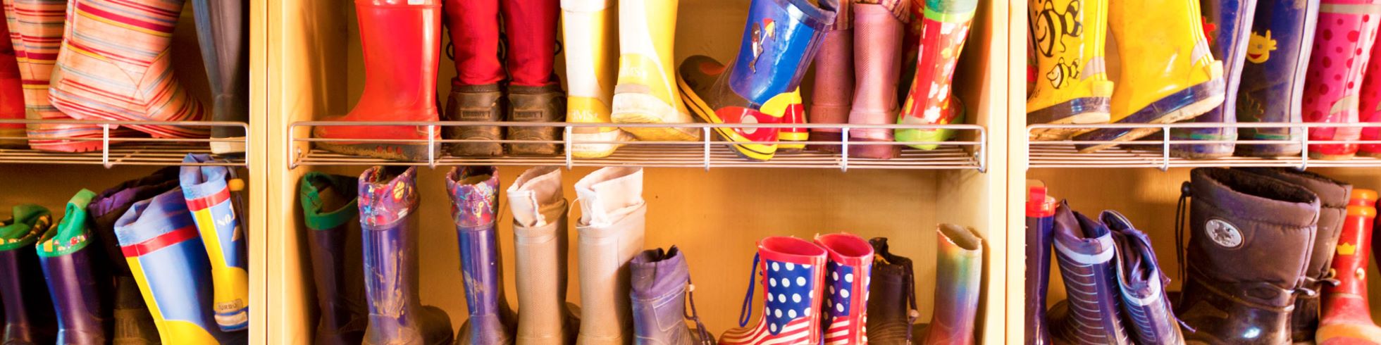 Viele bunte Gummistiefel von Kindern, die in einem Regal stehen.