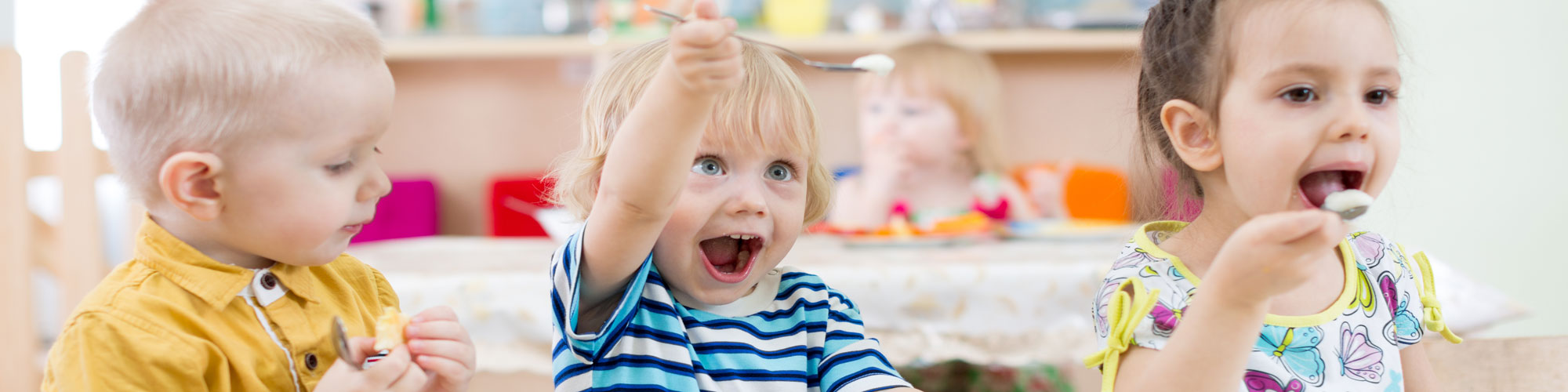 Drei Krippenkinder sitzen im Kindergarten am Tisch und essen.
