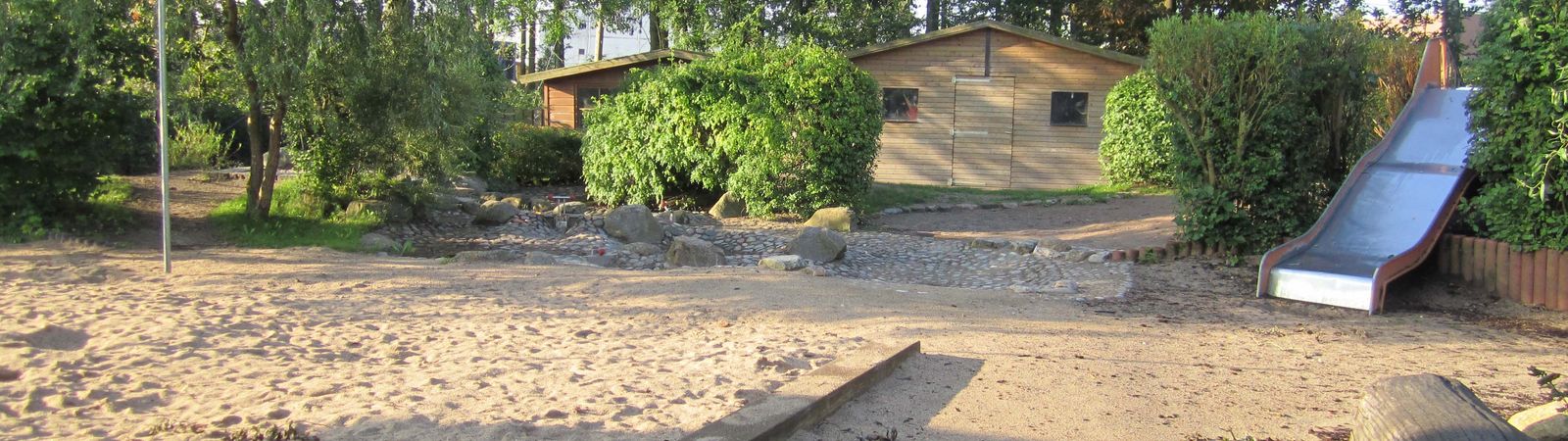 Große Sandfläche, eine Rutsche und mehrere Büsche und Baue