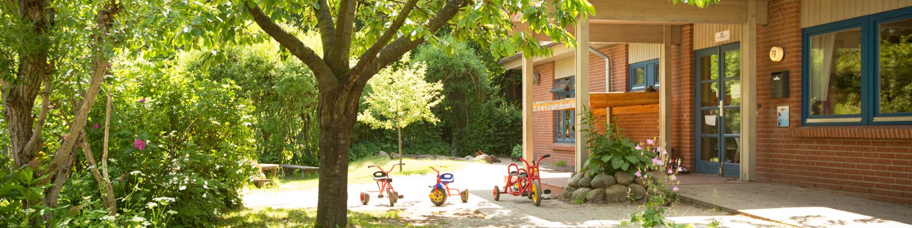 Sonne durchstrahlter Garten mit einem hölzernen Kitagebäude mittendrinnen.