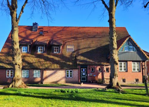 Rotes Backsteinhaus im Grünen mit zwei Bäumen davor.