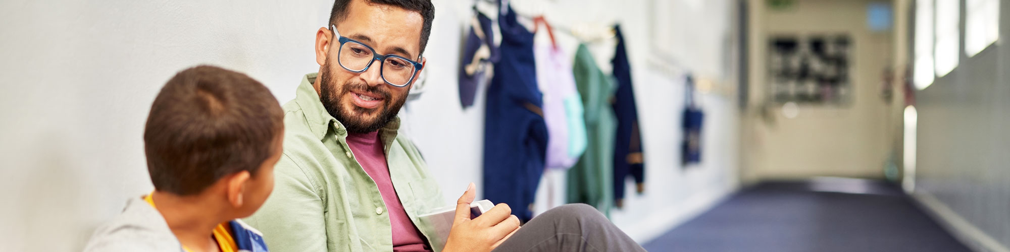 Ein Erzieher sitzt mit einem Kind auf dem Boden im Flur und sie unterhalten sich.