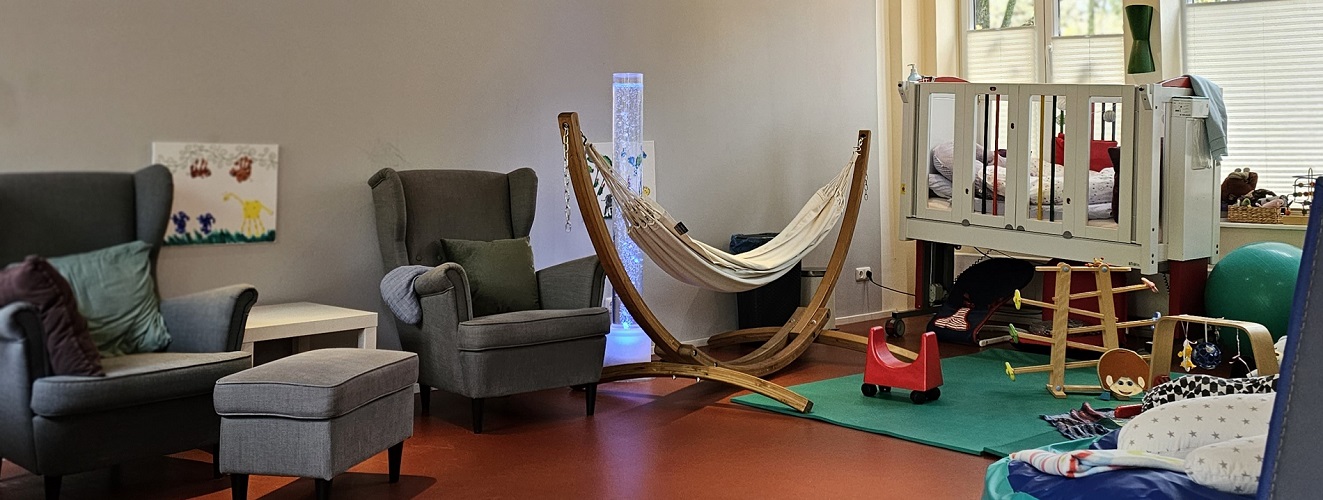 Kita Raum mit zwei Sesseln, Hängematte aus Holz und ein Kinderbett.